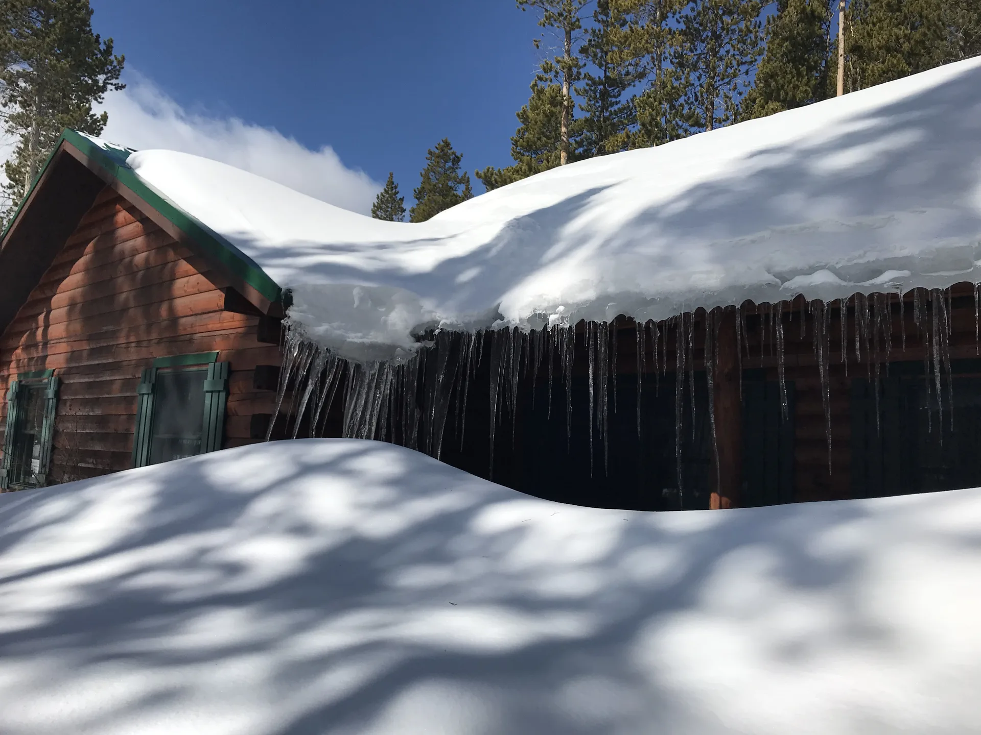 Heavy winter snow on the cabin roof with a row of icicles